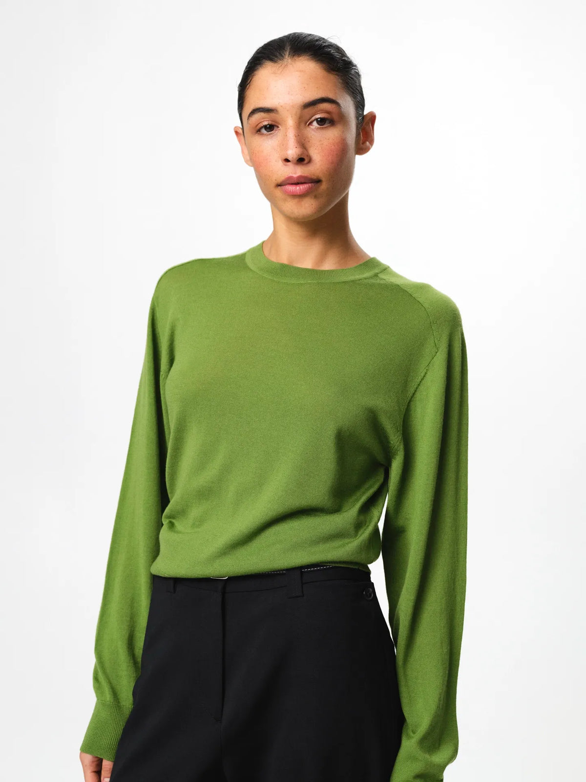 Julie Josephine Hanne Sweater Tulip Green: modern wardrobe essential classic round neck sweater knitted from 100% merino wool for lightweight warmth and a soft luxurious feel, shown in tulip green and styled to wear on its own or layered with a t shirt underneath, note that it fits small so taking one size up gives a more relaxed fit.