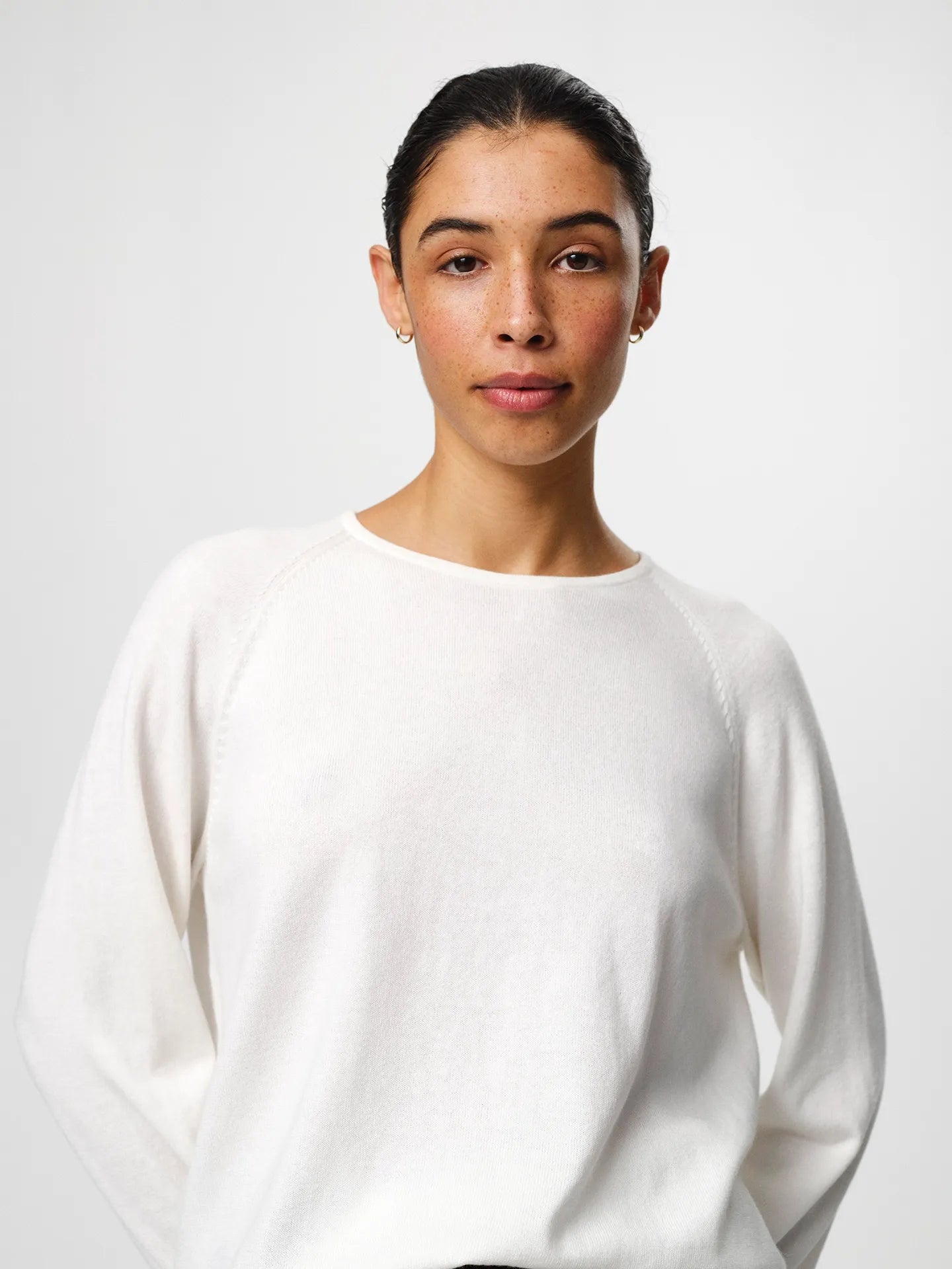 Julie Josephine Kate Roundneck Sweater Off White: product image of a soft, lightweight knit sweater in an off white shade, made from a wool and cotton blend that combines warmth with breathability, designed with a relaxed silhouette, long sleeves, subtle dropped shoulders, and a clean neckline, styled for easy everyday layering over a T shirt or worn on its own with tailored trousers or denim.